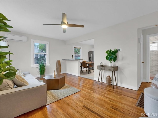 living area featuring ceiling fan, baseboards, wood finished floors, and a wall mounted AC