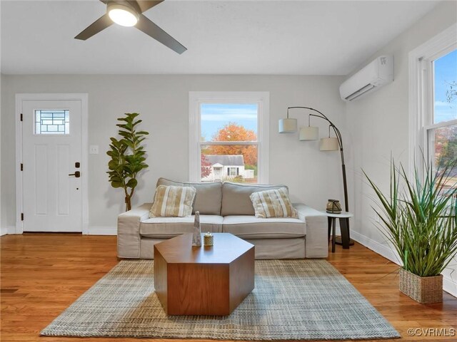 living room with a wall unit AC, wood finished floors, a ceiling fan, and baseboards