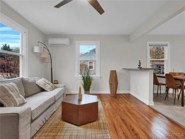 living area with a wall unit AC, wood finished floors, a wealth of natural light, and baseboards