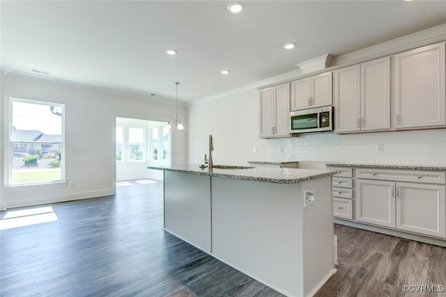 kitchen with dark wood-style flooring, a sink, light stone countertops, tasteful backsplash, and stainless steel microwave