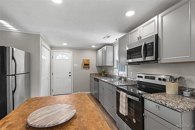 kitchen with gray cabinetry, a sink, dark stone countertops, a textured ceiling, and stainless steel appliances