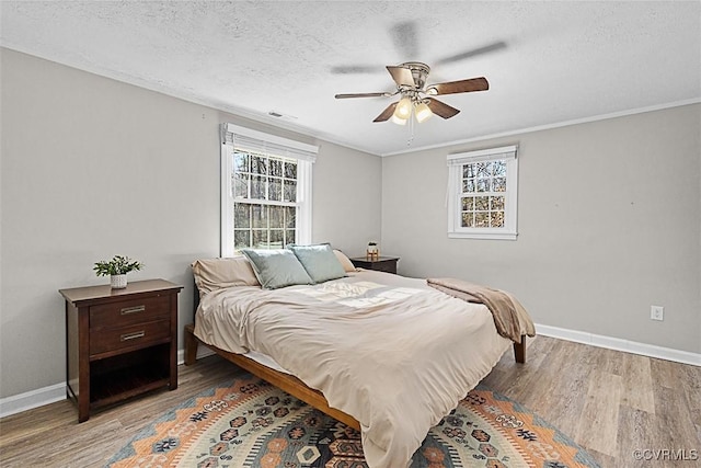 bedroom with visible vents, a ceiling fan, a textured ceiling, wood finished floors, and baseboards