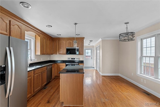 kitchen with a center island, stainless steel appliances, hanging light fixtures, ornamental molding, and wood finished floors