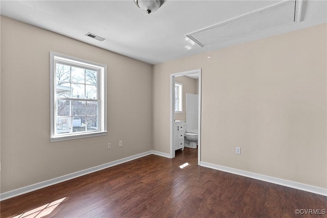 unfurnished bedroom with attic access, baseboards, visible vents, ensuite bath, and dark wood-type flooring