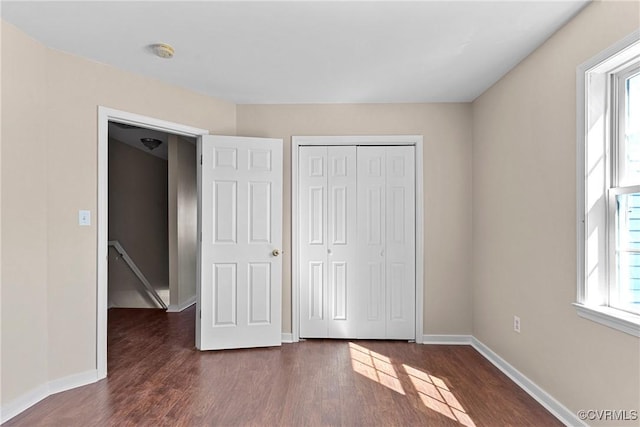 unfurnished bedroom with dark wood-type flooring, a closet, and baseboards