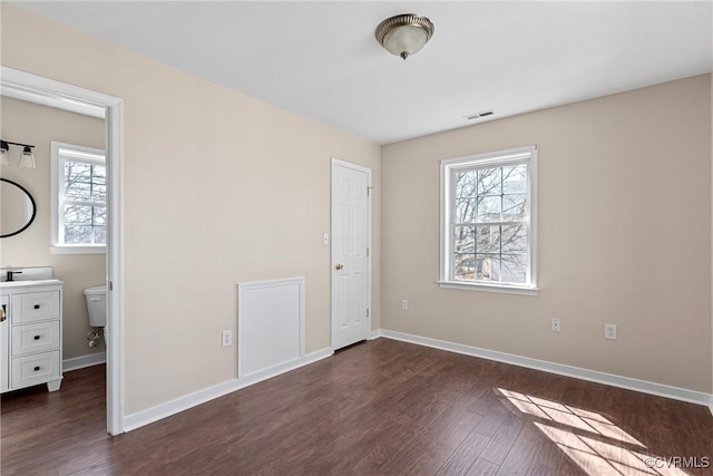 unfurnished bedroom featuring multiple windows, dark wood finished floors, visible vents, and baseboards