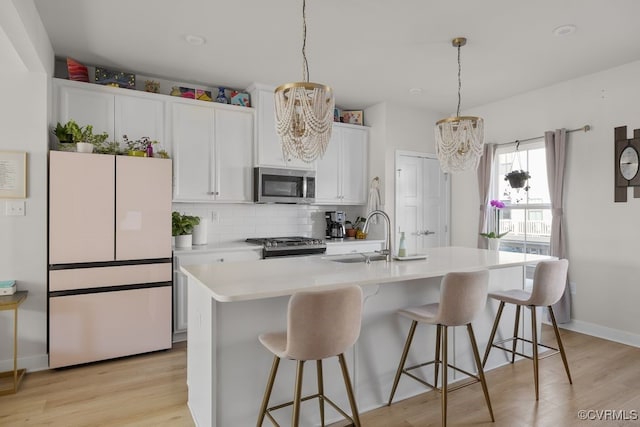 kitchen with light wood finished floors, decorative backsplash, stainless steel appliances, light countertops, and a sink