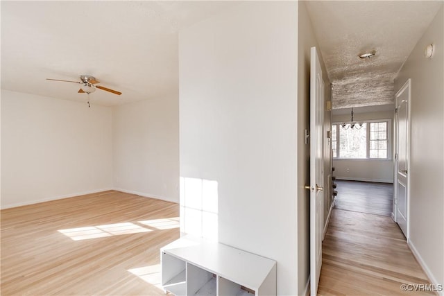 hall featuring light wood-type flooring, a textured ceiling, and baseboards