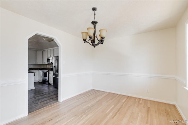 unfurnished dining area featuring light wood finished floors, baseboards, arched walkways, and an inviting chandelier