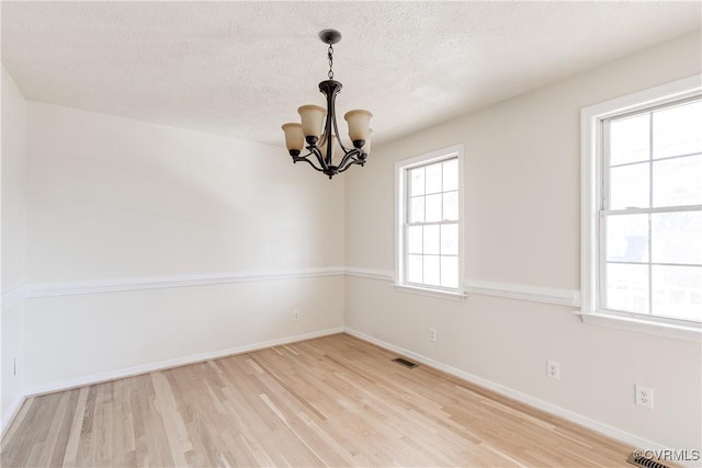 empty room with a textured ceiling, a chandelier, visible vents, baseboards, and light wood-style floors