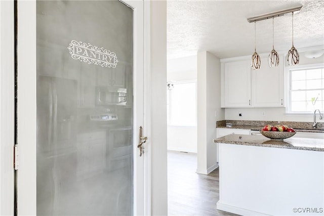 kitchen featuring stone countertops, wood finished floors, a textured ceiling, white cabinetry, and a sink