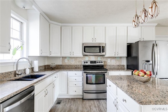 kitchen with a sink, white cabinets, appliances with stainless steel finishes, light stone countertops, and light wood finished floors