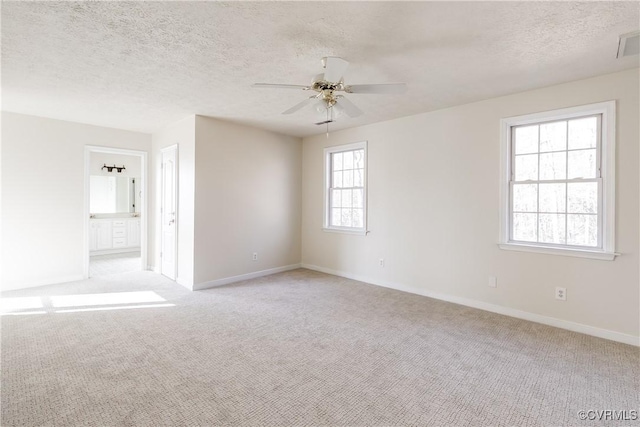 empty room with light colored carpet, ceiling fan, a textured ceiling, and baseboards