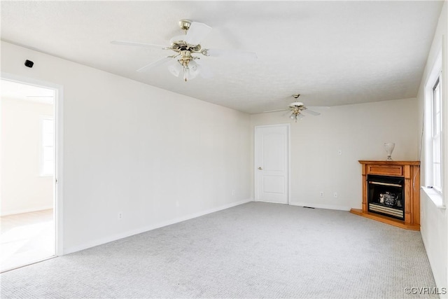 unfurnished living room with a fireplace with raised hearth, light carpet, a ceiling fan, and baseboards