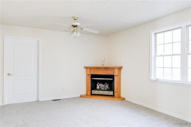 unfurnished living room with a fireplace with raised hearth, carpet flooring, visible vents, and a healthy amount of sunlight