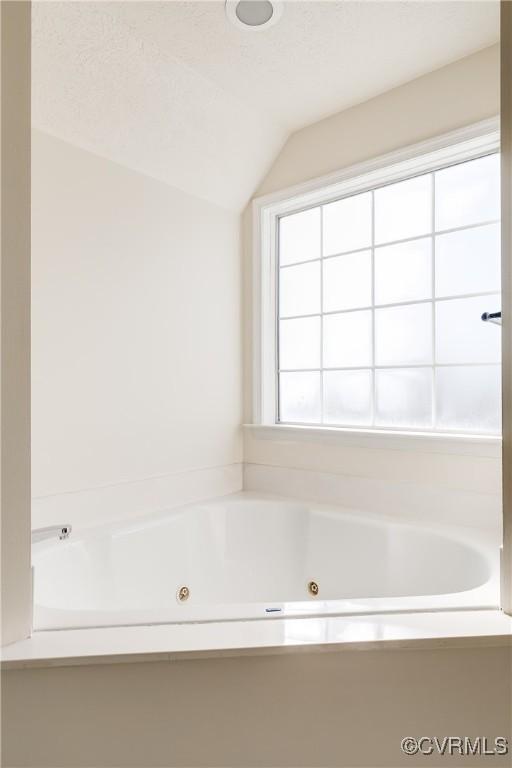 bathroom featuring lofted ceiling, a jetted tub, and a textured ceiling