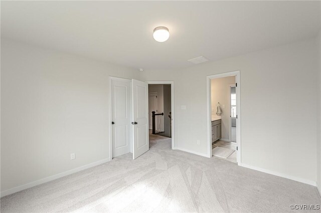 unfurnished bedroom featuring baseboards, ensuite bathroom, and light colored carpet