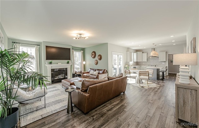living room featuring dark wood-type flooring, recessed lighting, a glass covered fireplace, and a healthy amount of sunlight