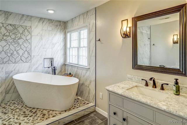 full bathroom with vanity, tile walls, and a freestanding tub