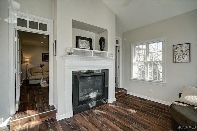 living room with visible vents, baseboards, wood tiled floor, vaulted ceiling, and a glass covered fireplace