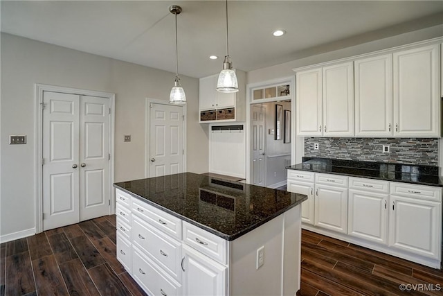 kitchen with wood finish floors, dark stone counters, white cabinets, tasteful backsplash, and a center island