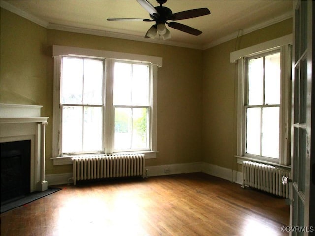 unfurnished living room with radiator heating unit, a fireplace, wood finished floors, and crown molding