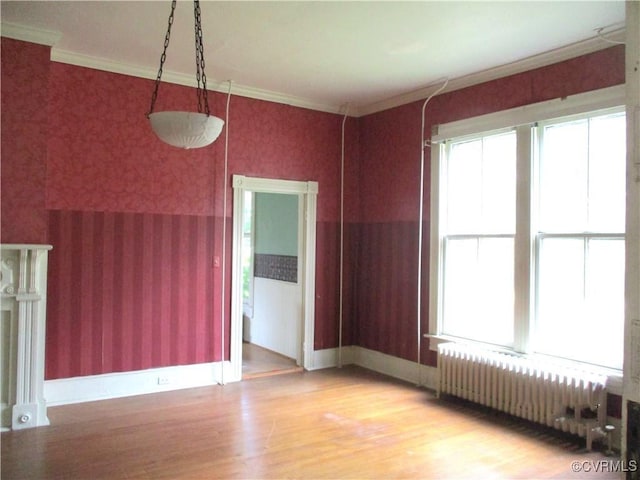 spare room with wallpapered walls, baseboards, radiator heating unit, light wood-style flooring, and crown molding