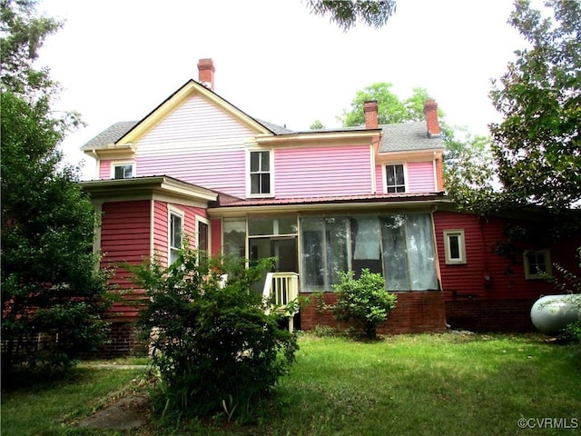 rear view of house featuring a lawn, a chimney, and a sunroom