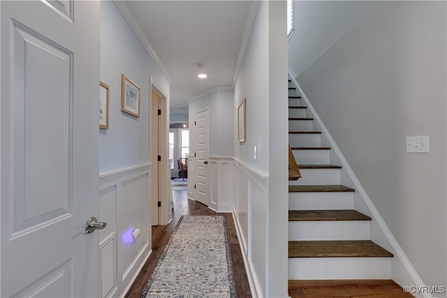 stairway featuring recessed lighting, a decorative wall, wood finished floors, ornamental molding, and wainscoting