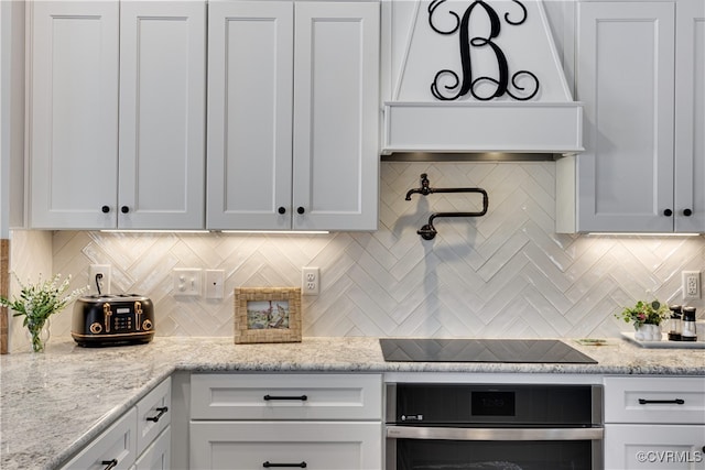 kitchen with decorative backsplash, oven, custom exhaust hood, black electric stovetop, and white cabinetry