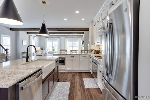 kitchen with appliances with stainless steel finishes, a wealth of natural light, dark wood finished floors, and light stone countertops