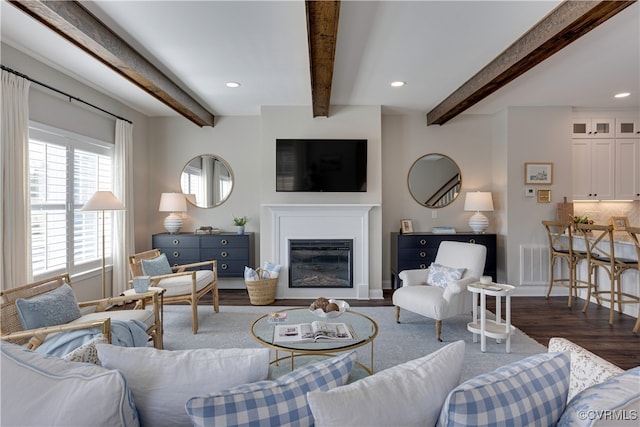 living room featuring visible vents, a glass covered fireplace, dark wood-style floors, beamed ceiling, and recessed lighting