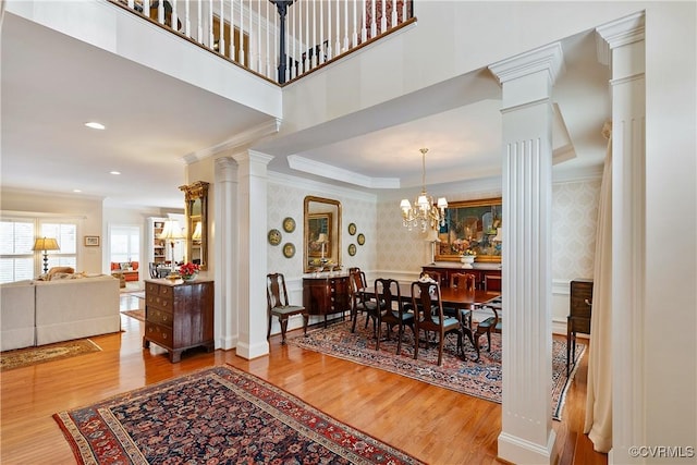 dining space featuring ornate columns, ornamental molding, wood finished floors, and wallpapered walls