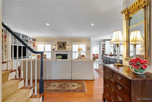 living room with recessed lighting, a fireplace, wood finished floors, stairs, and crown molding