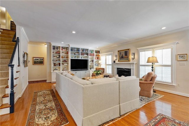 living area featuring light wood-style flooring, stairway, a high end fireplace, and crown molding