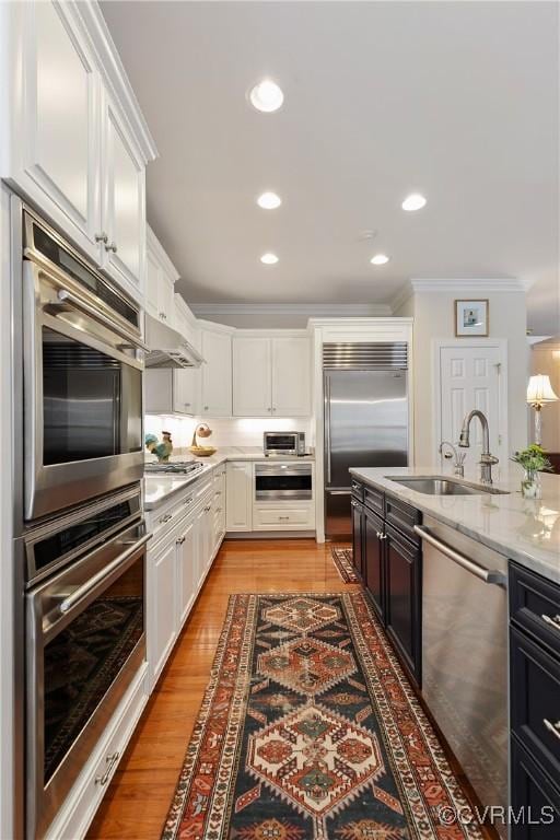 kitchen with light wood-style flooring, ornamental molding, stainless steel appliances, white cabinetry, and a sink