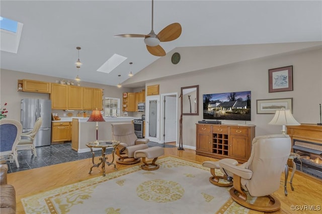 living area featuring vaulted ceiling with skylight, ceiling fan, and baseboards