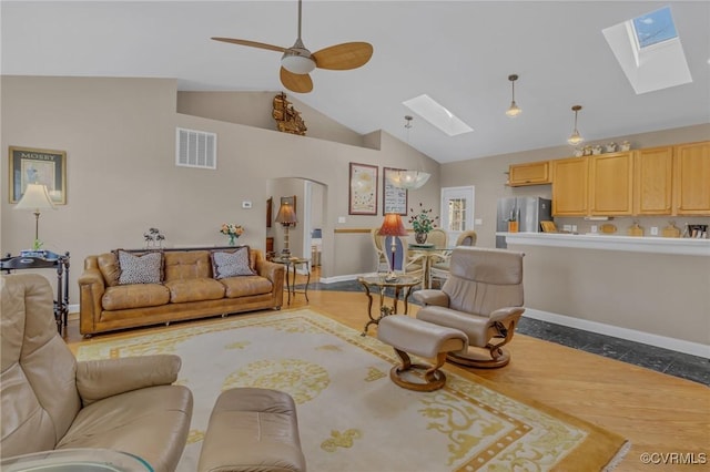 living room with a skylight, visible vents, ceiling fan, high vaulted ceiling, and baseboards