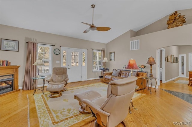 living room with visible vents, arched walkways, a glass covered fireplace, wood finished floors, and a wealth of natural light