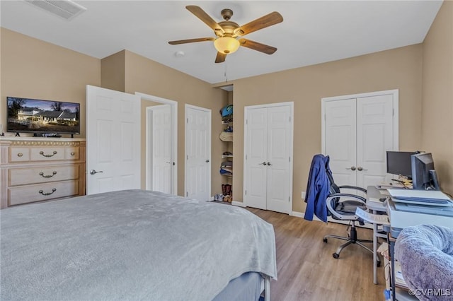 bedroom featuring light wood-style flooring, visible vents, baseboards, a ceiling fan, and two closets