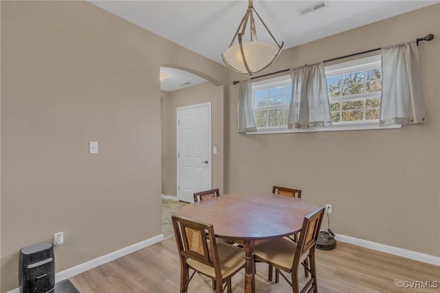 dining room with arched walkways, light wood-style floors, visible vents, and baseboards