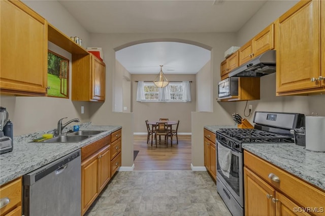 kitchen featuring baseboards, arched walkways, stainless steel appliances, under cabinet range hood, and a sink