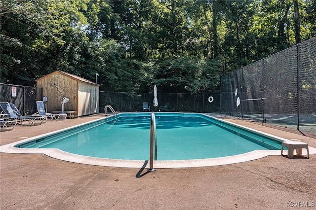 community pool with a patio area, fence, a storage unit, and an outdoor structure