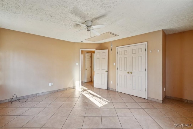 unfurnished bedroom featuring light tile patterned floors, a closet, a textured ceiling, and attic access