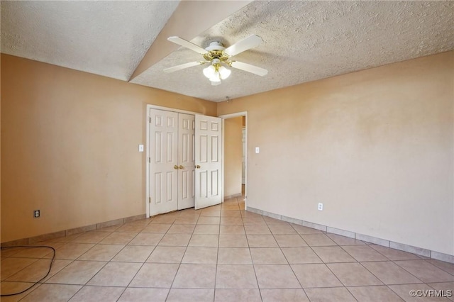 empty room featuring light tile patterned floors, a textured ceiling, baseboards, and a ceiling fan