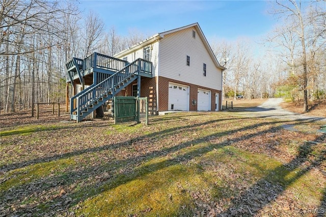 view of property exterior with a garage, brick siding, stairs, driveway, and a wooden deck