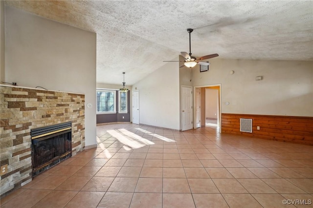 unfurnished living room with visible vents, a glass covered fireplace, ceiling fan with notable chandelier, a textured ceiling, and light tile patterned flooring