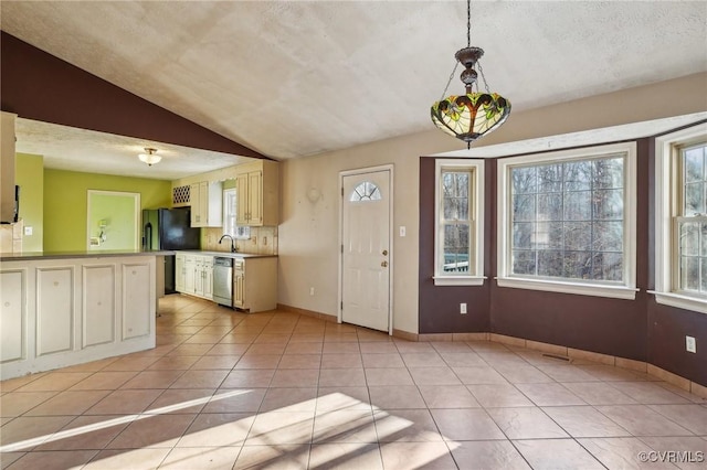 kitchen featuring cream cabinetry, light tile patterned floors, lofted ceiling, stainless steel dishwasher, and freestanding refrigerator