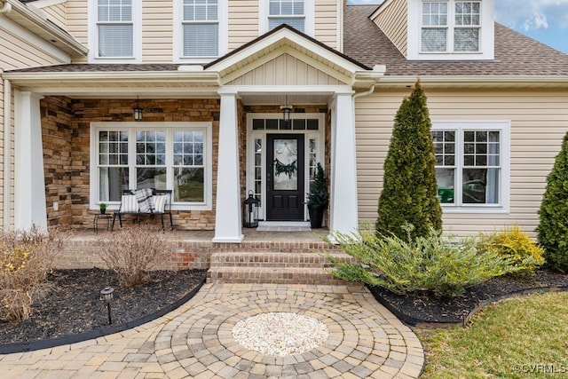 property entrance featuring a porch, stone siding, and roof with shingles