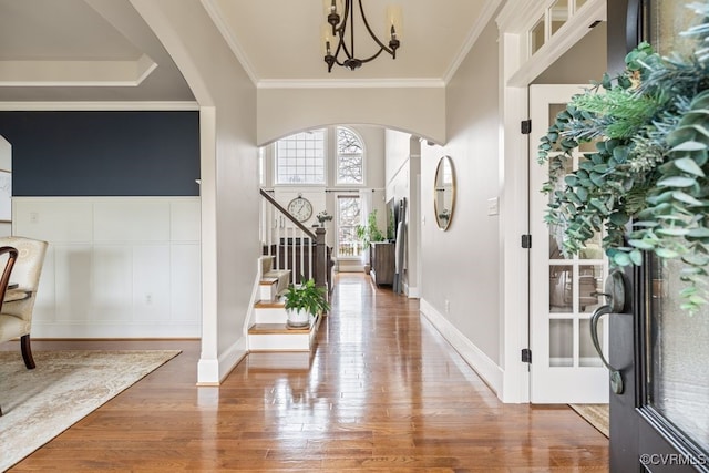 entryway with crown molding, arched walkways, wood finished floors, and a notable chandelier